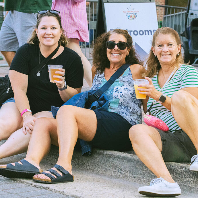 Three women sitting on the curb enjoying the festivities