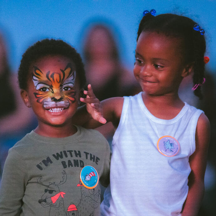 A young girl admiring a young boy's tiger face paint